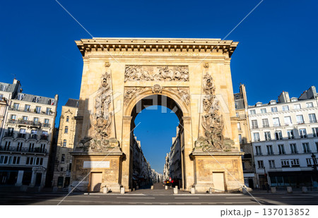 Scenic sunny view of the historic Porte Saint-Denis triumphal arch with intricate bas-relief carvings and classical Parisian buildings in Paris, France. Scenic sunny view of the historic Porte Saint-Denis triumphal arch with intricate bas-relief carvings and classical Parisian buildings in Paris, France. 137013852