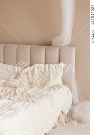 Unmade white bed with beige upholstered headboard and sheer canopy in minimalist bedroom Unmade white bed with beige upholstered headboard and sheer canopy in minimalist bedroom 137014027