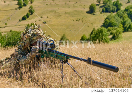 Sniper Soldier In Ghillie Suit Aiming Suppressed Sniper Rifle In Grassland Field 137014103