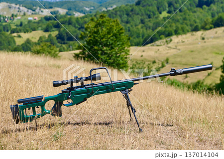 Bolt-Action Sniper Rifle With Scope and Suppressor On Bipod In Open Grassland Hunting Field Bolt-Action Sniper Rifle With Scope and Suppressor On Bipod In Open Grassland Hunting Field 137014104