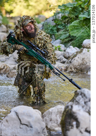 Soldier Sniper In Ghillie Suit Crossing Rocky River While Carrying Scoped Rifle During Recon Mission Soldier Sniper In Ghillie Suit Crossing Rocky River While Carrying Scoped Rifle During Recon Mission 137014106