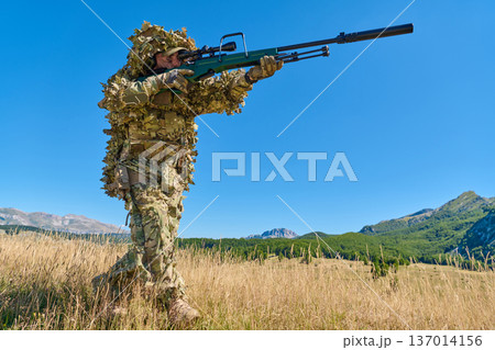 Sniper Soldier In Ghillie Suit With Rifle Patrolling Grassy Mountain Field On Clear Day 137014156