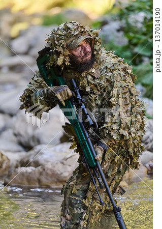 Sniper Soldier in Ghillie Suit With Rifle Crossing Stream During Camouflage Tactical Military Operation Sniper Soldier in Ghillie Suit With Rifle Crossing Stream During Camouflage Tactical Military Operation 137014190