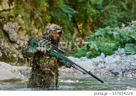 Sniper In Ghillie Suit Wading Through River With Camouflaged Sniper Rifle In Forest Ambush Sniper In Ghillie Suit Wading Through River With Camouflaged Sniper Rifle In Forest Ambush 137014229