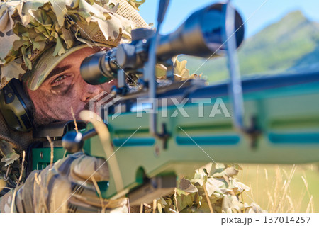 Sniper Soldier in Ghillie Suit Aiming Precision Rifle Through Scope in Sunlit Field 137014257