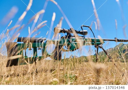 Sniper Rifle With Scope On Bipod Lying In Dry Grass In Open Mountain Field Sniper Rifle With Scope On Bipod Lying In Dry Grass In Open Mountain Field 137014346