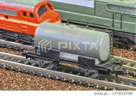 Close-up of a model train tank car on tracks with other trains in the background. Detailed view of a miniature gray tank car with intricate wheels and coupling, positioned on a model railway track Close-up of a model train tank car on tracks with other trains in the background. Detailed view of a miniature gray tank car with intricate wheels and coupling, positioned on a model railway track 137014799