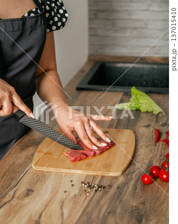 Girl cuts meat with a knife on a wooden board. Kitchen location. Girl cuts meat with a knife on a wooden board. Kitchen location. 137015410