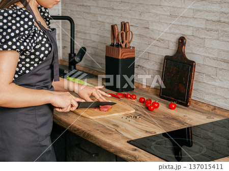 Girl cuts meat with a knife on a wooden board. Kitchen location. 137015411
