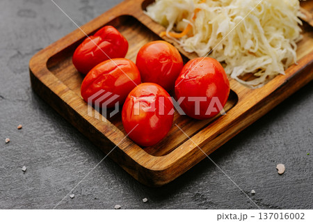 Pickled tomatoes and fermented cabbage served on rustic wooden board close up Pickled tomatoes and fermented cabbage served on rustic wooden board close up 137016002