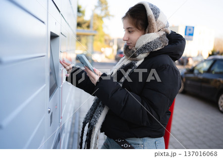 Young Girl Opens Outdoor Parcel Locker On A Street Using A Smartphone Young Girl Opens Outdoor Parcel Locker On A Street Using A Smartphone 137016068
