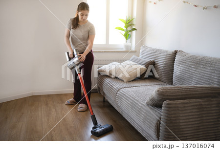 Young girl vacuums the floor in a living room during the day Young girl vacuums the floor in a living room during the day 137016074