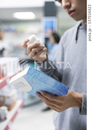 Close up of male customer comparing capsule and pill medications while carefully reading packaging information in pharmacy aisle. Man selects most suitable sleep aid at local dispensary. 137016823