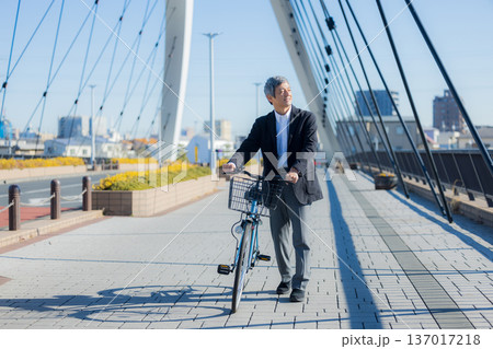 自転車を押して歩く60代男性 137017218
