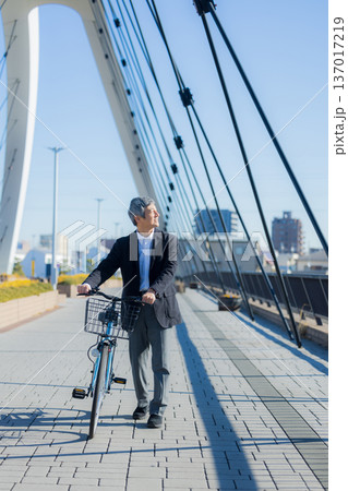 自転車を押して歩く60代男性 137017219