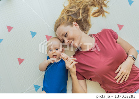 Mother and baby lying on a soft play mat at home, playing, talking and sharing a joyful moment together. Authentic family lifestyle, early childhood development and emotional bonding. Parenting and 137018293