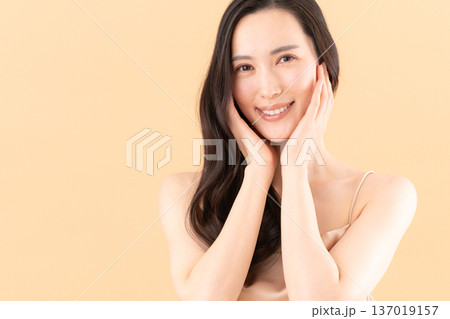 ベージュ背景でスキンケアをする女性のビューティーイメージ 137019157