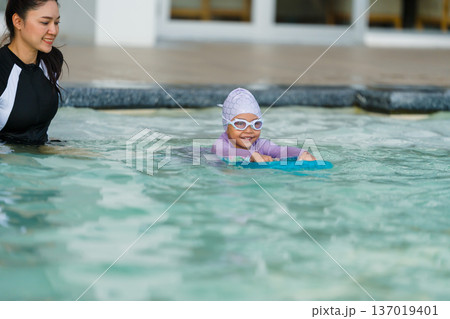 preschool child girl learning to swim with board with mother in swimming pool 137019401