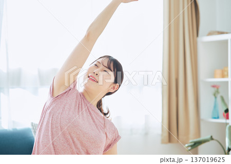 自宅で体をほぐすストレッチをする30代女性の健康習慣 自宅で体をほぐすストレッチをする30代女性の健康習慣 137019625