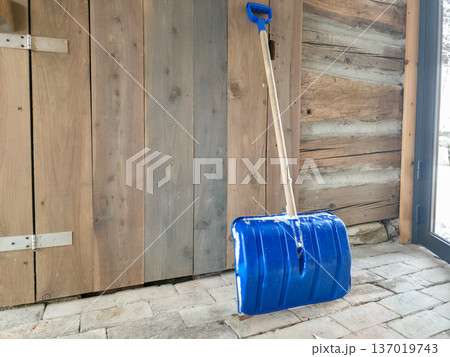 A snow shovel is leaning against a wooden wall. Precipitation in winter requires clearing during snowfall. High quality photo 137019743