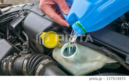 A man is pouring windshield washer fluid into the car's reservoir. Preparing for a road trip. High quality photo 137019855