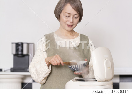 キッチンで炊飯器から炊きたてご飯を茶碗によそうシニア女性 137020314