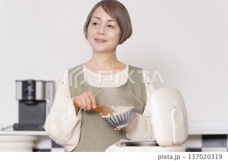 キッチンで炊飯器から炊きたてご飯を茶碗によそうシニア女性 137020319