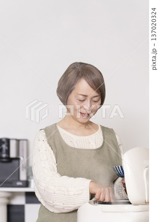 キッチンで炊飯器から炊きたてご飯を茶碗によそうシニア女性 キッチンで炊飯器から炊きたてご飯を茶碗によそうシニア女性 137020324