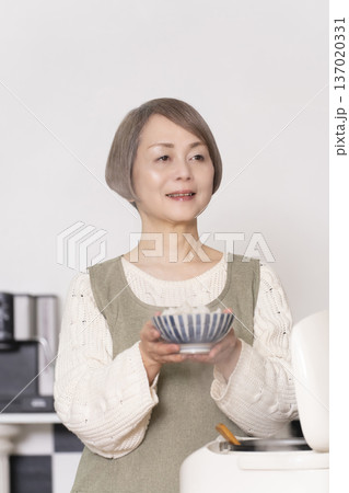 キッチンで炊飯器から炊きたてご飯を茶碗によそうシニア女性 137020331