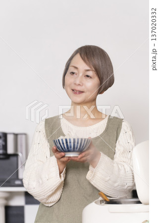 キッチンで炊飯器から炊きたてご飯を茶碗によそうシニア女性 137020332
