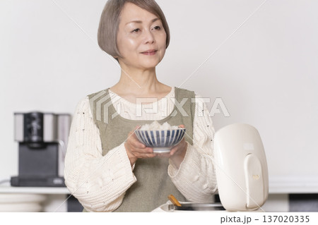 キッチンで炊飯器から炊きたてご飯を茶碗によそうシニア女性 137020335