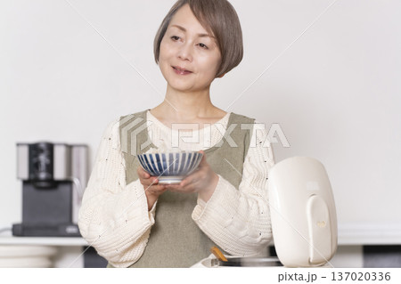キッチンで炊飯器から炊きたてご飯を茶碗によそうシニア女性 キッチンで炊飯器から炊きたてご飯を茶碗によそうシニア女性 137020336