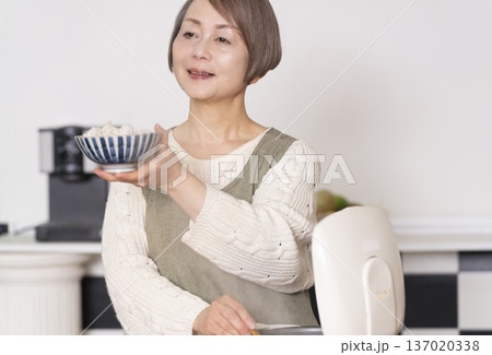 キッチンで炊飯器から炊きたてご飯を茶碗によそうシニア女性 キッチンで炊飯器から炊きたてご飯を茶碗によそうシニア女性 137020338