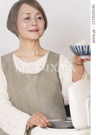 キッチンで炊飯器から炊きたてご飯を茶碗によそうシニア女性 137020340