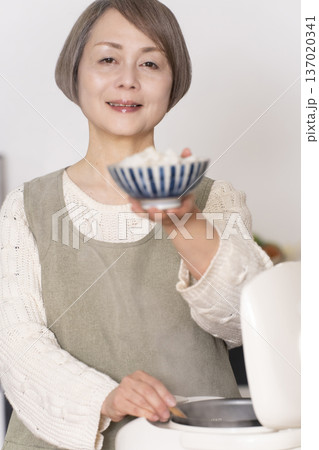 キッチンで炊飯器から炊きたてご飯を茶碗によそうシニア女性 137020341