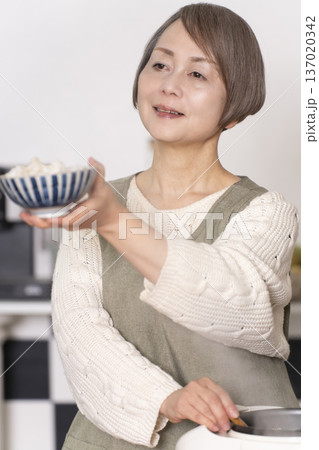 キッチンで炊飯器から炊きたてご飯を茶碗によそうシニア女性 137020342