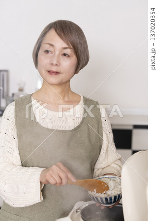 キッチンで炊飯器から炊きたてご飯を茶碗によそうシニア女性 137020354