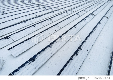 Aerial view of snow covered sustainable electric power plant with rows of solar photovoltaic panels for producing clean electrical energy. Low effectivity of renewable electricity in northern winter 137020423