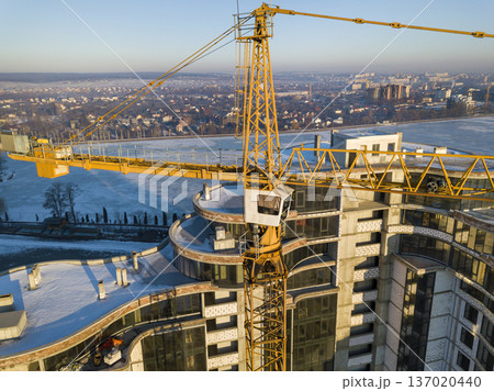 Apartment or office tall building under construction, top view. Tower crane on bright blue sky copy space background, city landscape stretching to horizon. Drone aerial photography. 137020440