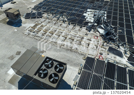 Aerial view of damaged by hurricane wind photovoltaic solar panels mounted on industrial building roof for producing green ecological electricity. Consequences of natural disaster 137020454