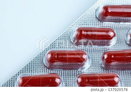 Close-up of red pharmaceutical capsules in a silver foil blister pack on a white background Close-up of red pharmaceutical capsules in a silver foil blister pack on a white background 137020576