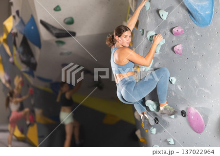 Girl in sportswear practicing rock climbing on climbing wall 137022964