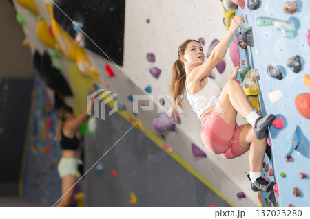 Sportive girl climbing on artificial rock wall in rock climbing gym Sportive girl climbing on artificial rock wall in rock climbing gym 137023280