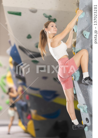 Girl climbs artificial wall bouldering, working out in gym Girl climbs artificial wall bouldering, working out in gym 137023281