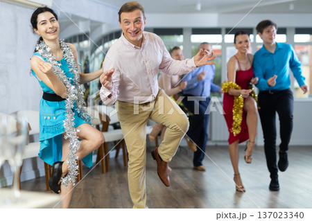 Cheerful man dancing jive with young brunette during corporate Christmas party 137023340