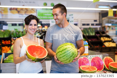 Positive couple choosing watermelon in fruit and vegetable section of supermarket Positive couple choosing watermelon in fruit and vegetable section of supermarket 137023365