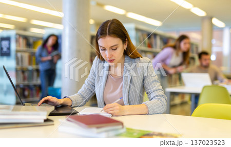 Portrait of woman with laptop and book in public library closeup Portrait of woman with laptop and book in public library closeup 137023523