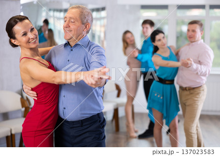 Happy people of different ages dancing tango in pairs in dance hall Happy people of different ages dancing tango in pairs in dance hall 137023583