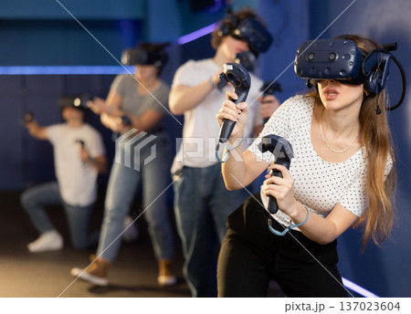 Young woman in VR glasses playing virtual game with handheld controllers 137023604