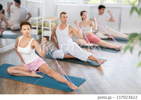 Young men and women doing arm workout with band sitting one leg extended 137023622